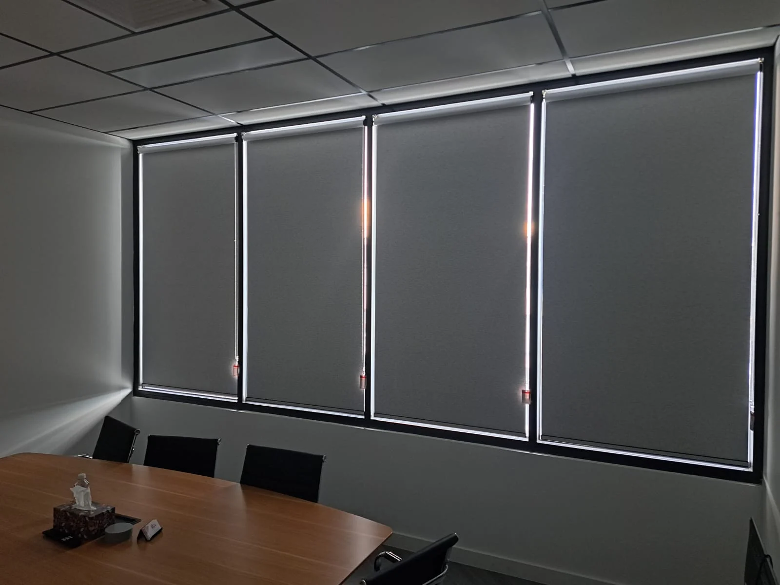 Three lowered grey roller blinds across an office window